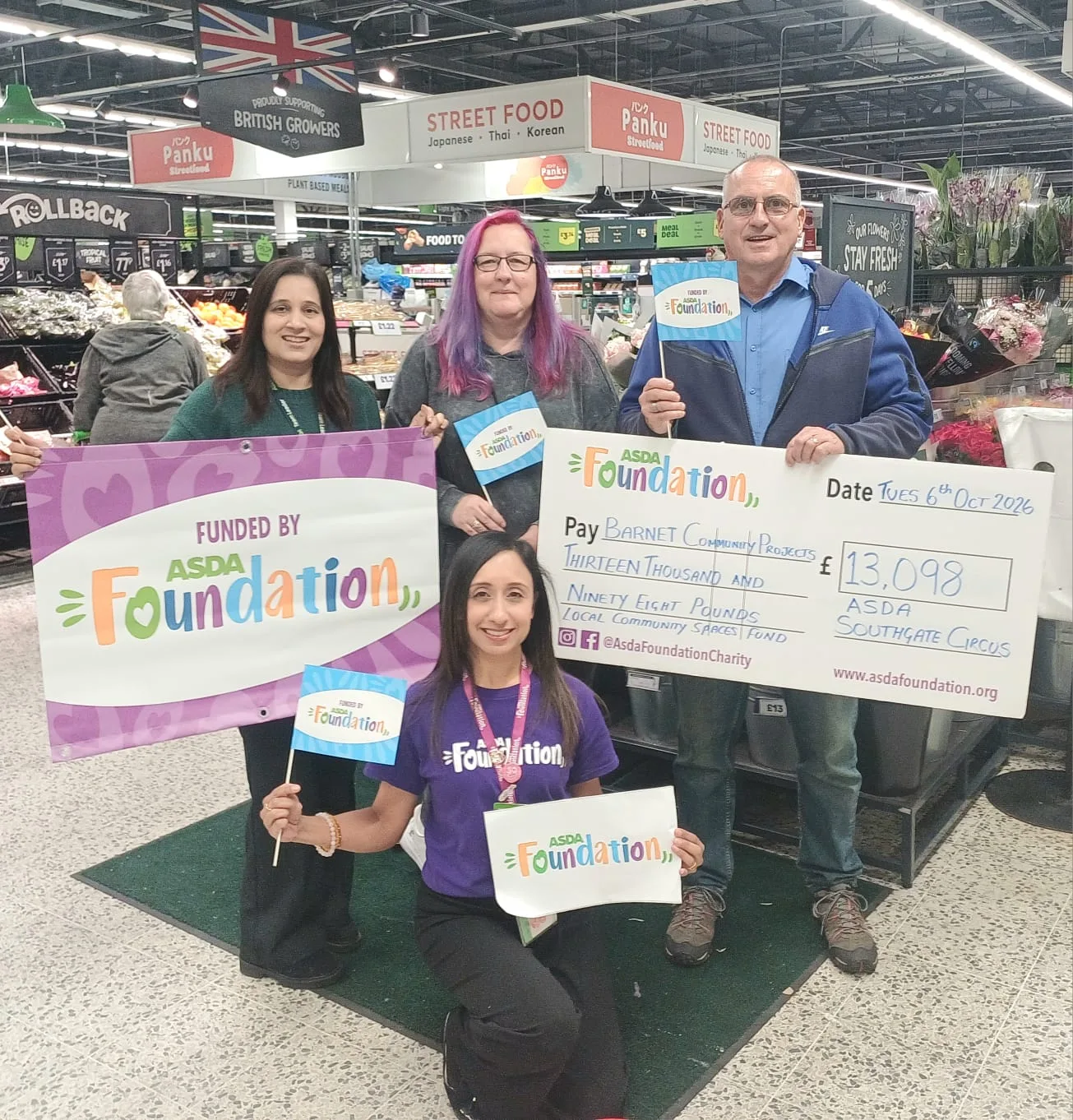 Four people on the shop floor of Asda Southgate Circus, two holding a Funded by Asda Foundation banner and a large cheque made out to Barnet Community Projects for £13,098, one kneeling at the front with an Asda Foundation sign